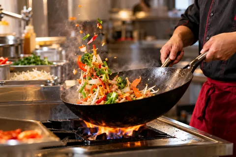 Koch schwenkt Gemüse im Wok über der Flamme